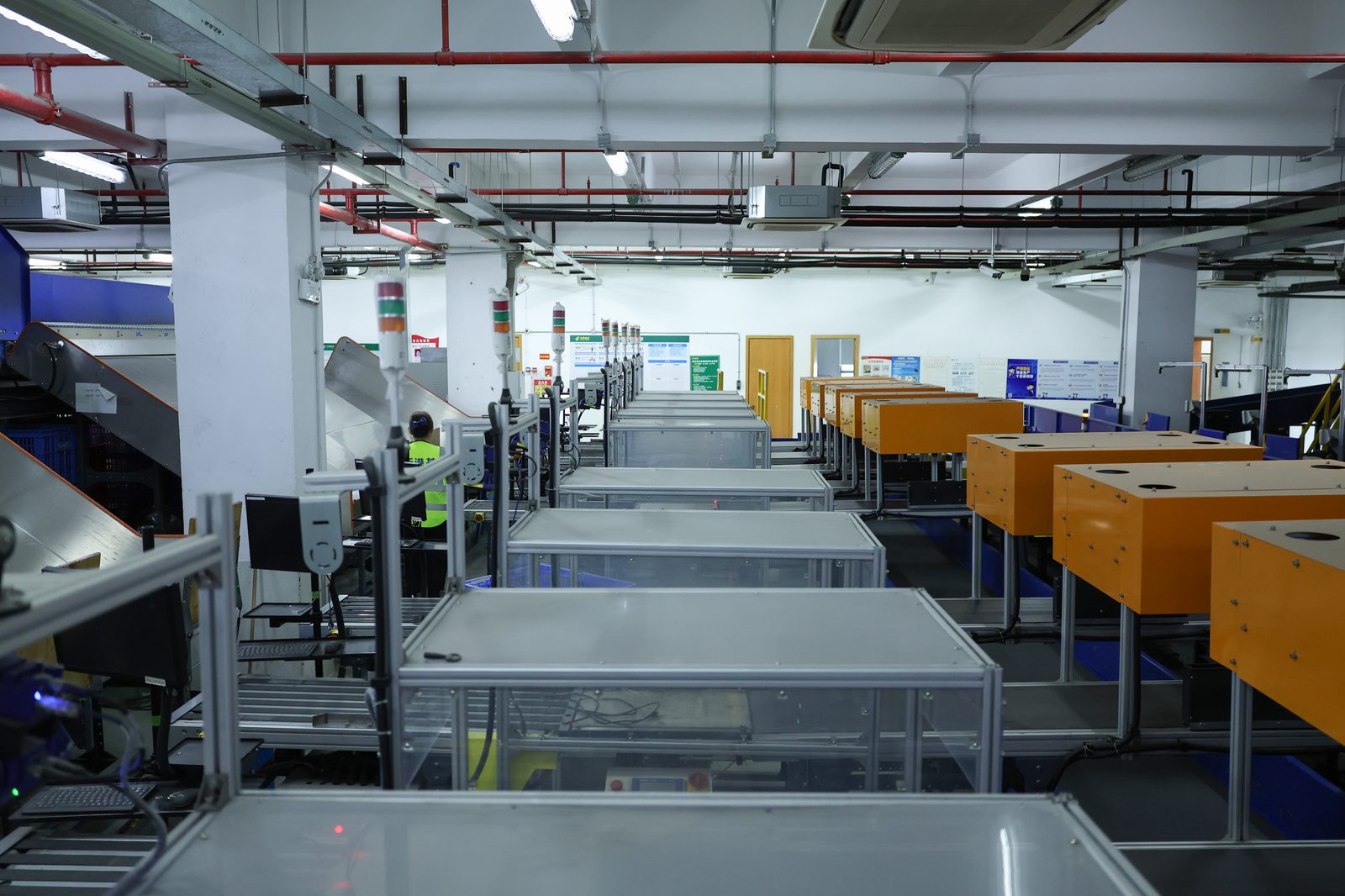 An automated parcel sortation line: rows of aluminium-framed chutes topped with status lights, feeding orange collection bins on the right.