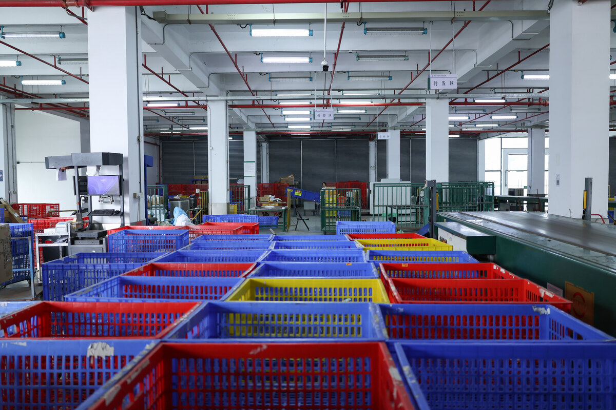 Rows of red, blue and yellow sorting baskets beside a warehouse conveyor.