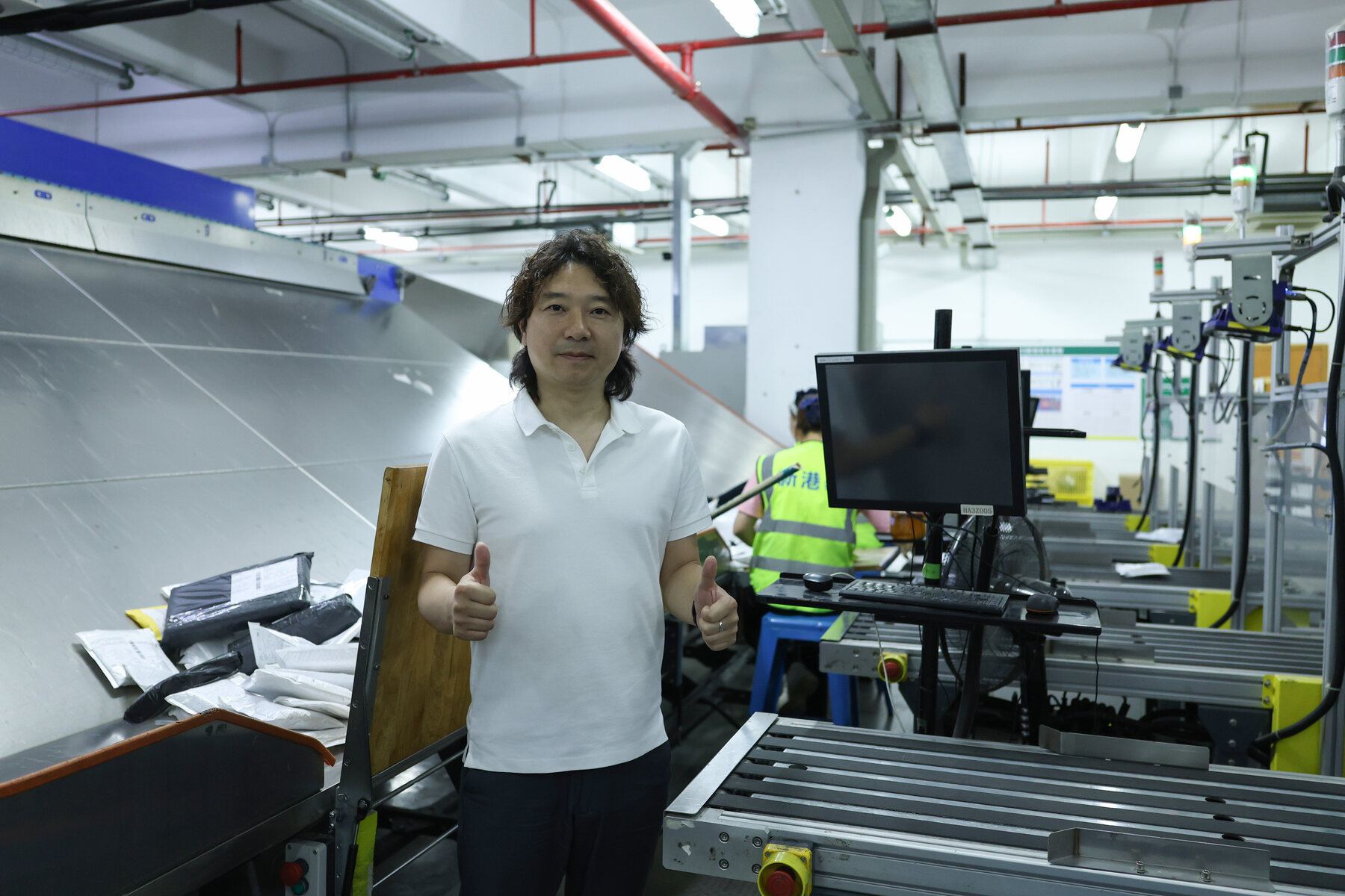 ASG team member presenting automated warehouse equipment, blue conveyor lanes, cameras, and parcel handling stations.