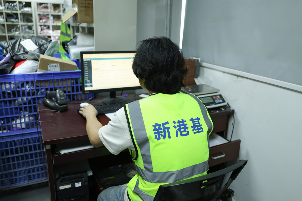 A warehouse operator in a high-visibility vest works at a computer beside storage baskets.