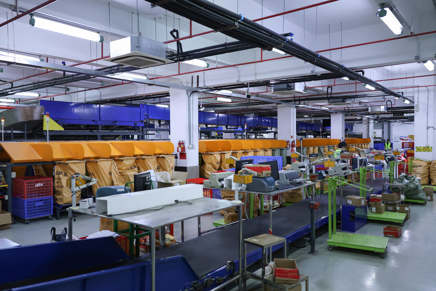 ASG sortation area with conveyors, worktables, bag chutes, crates and staff in the background.