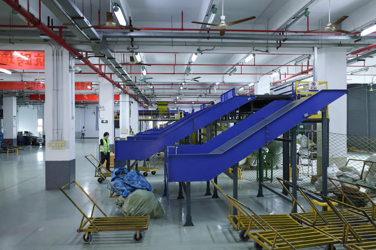 Blue outbound parcel chutes, yellow carts and parcel sacks in a sorting hall.