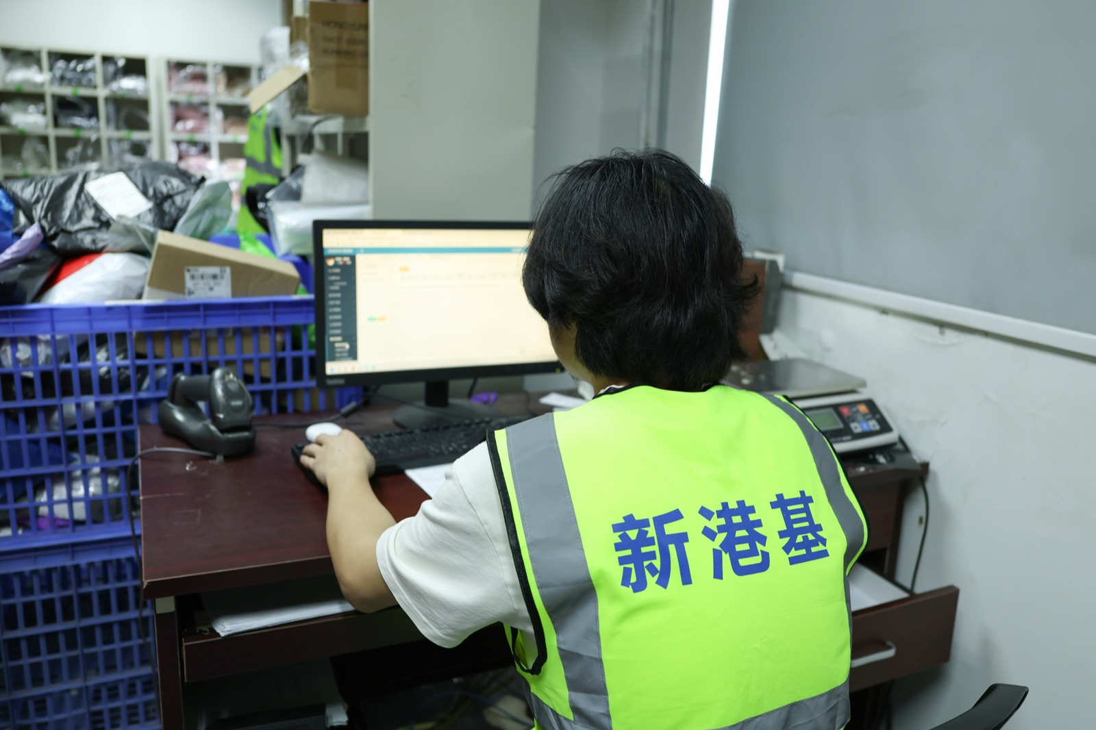 A warehouse worker using a computer terminal beside an operations area.