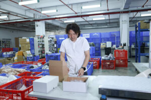 A person preparing an open carton at a warehouse packing bench.