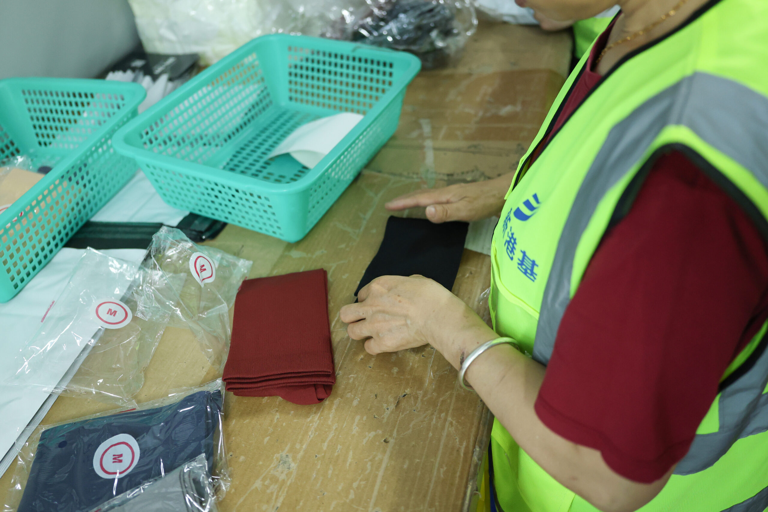 A warehouse worker examining folded fabric items beside labeled plastic packaging.
