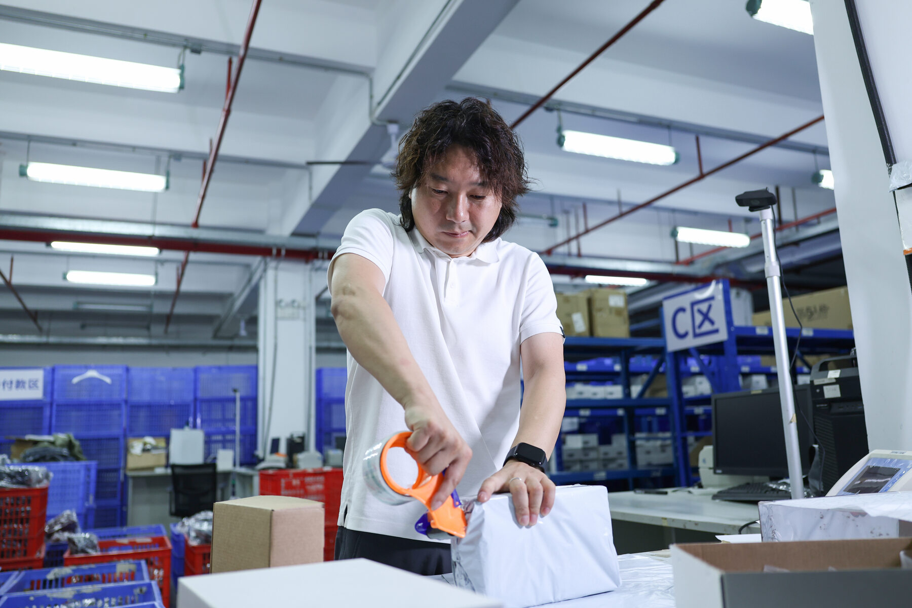 A man applying tape to a wrapped parcel at a warehouse workbench.