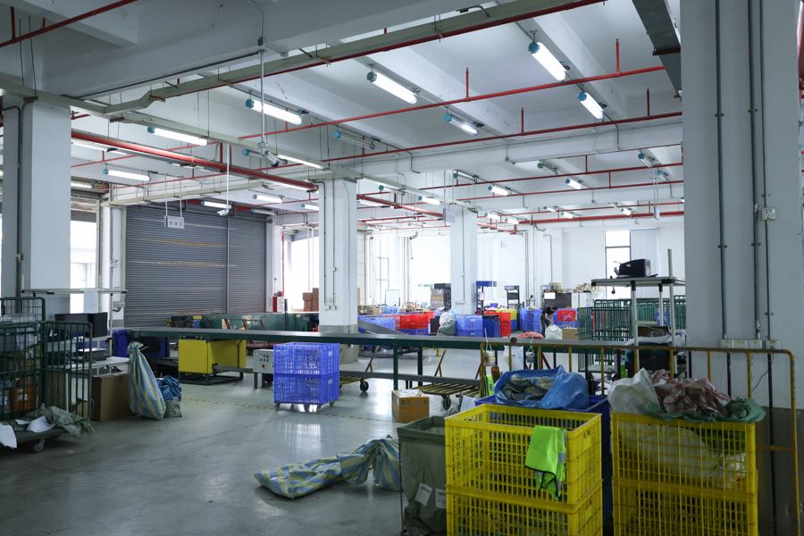 Warehouse floor with yellow and blue crates, large sacks and a long work bench