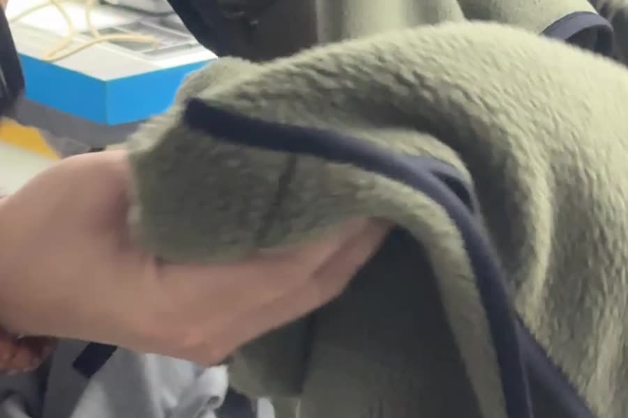 A hand folds olive fleece to show its dark binding edge.