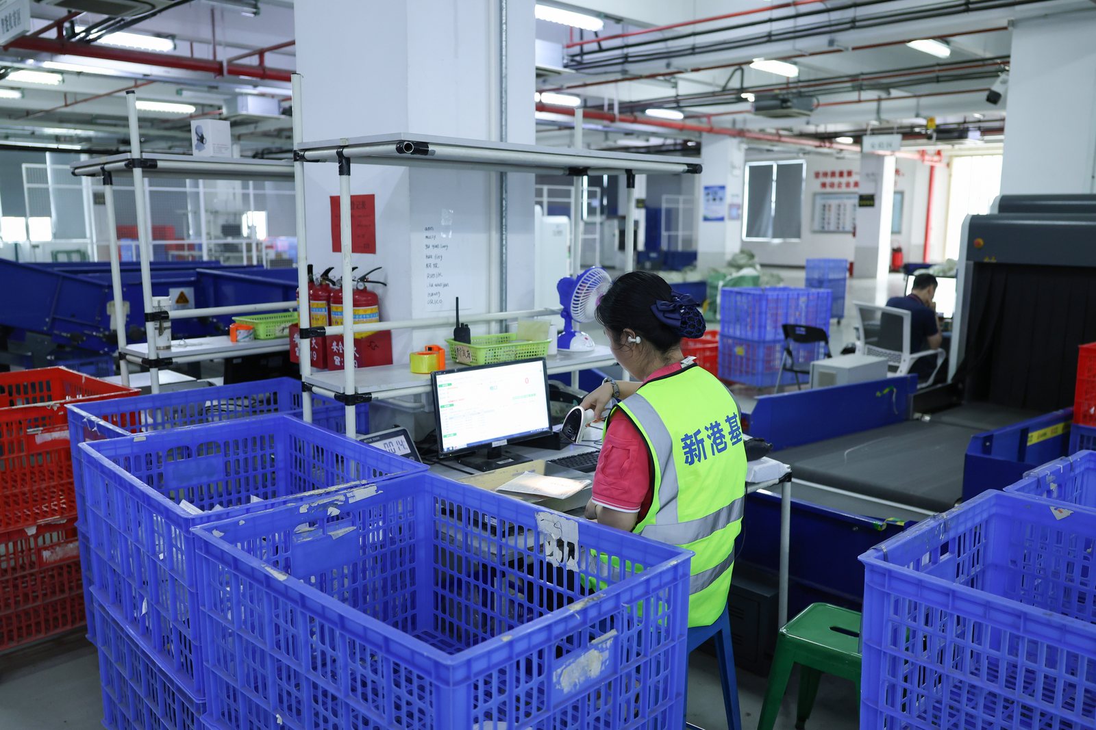ASG worker seated at a warehouse scanning workstation surrounded by blue parcel bins.